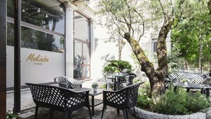 An outdoor seating area with black metal chairs and tables, a white planter with greenery, and a building with 'Mokinba hotels' signage. - Mokinba Hotels Montebianco (Milan)