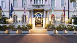 A hotel entrance with a sign reading "Molinba," flags, and a symmetrical facade with columns and arched windows. - Mokinba Hotels Montebianco (Milan)