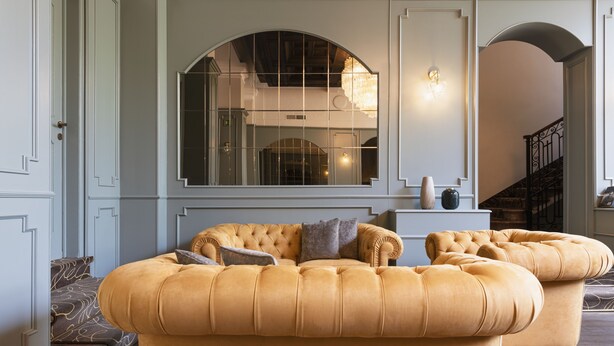 A spacious living area with a large arched window, a tufted sofa set, and a staircase leading to an upper floor. - Mokinba Hotels Montebianco (Milan)