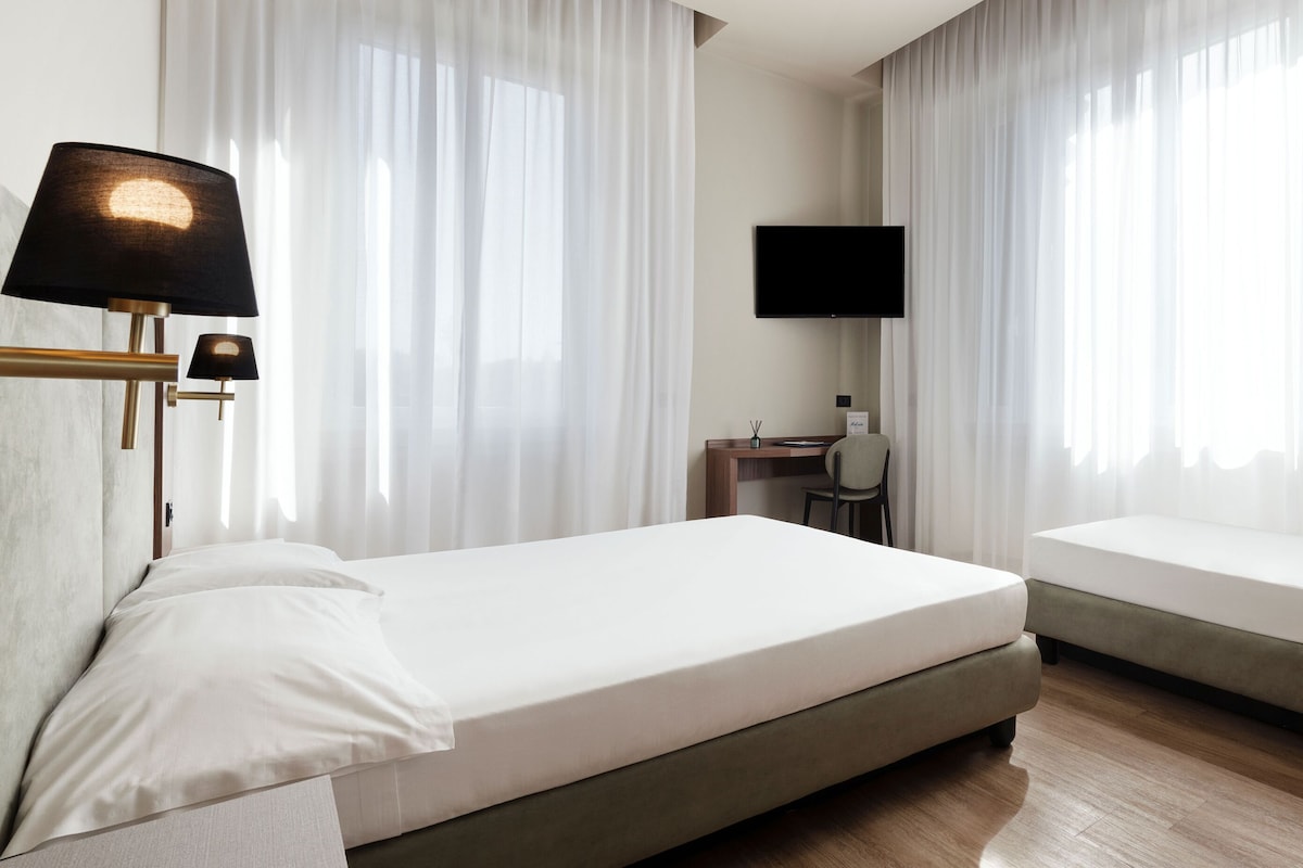 A hotel room with two beds, a desk, a chair, and a TV mounted on the wall.