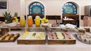 A breakfast buffet with various food items and beverages, including fruits, juices, and pastries, arranged on a table with a view of stained glass windows. - Mokinba Hotels Montebianco (Milan)
