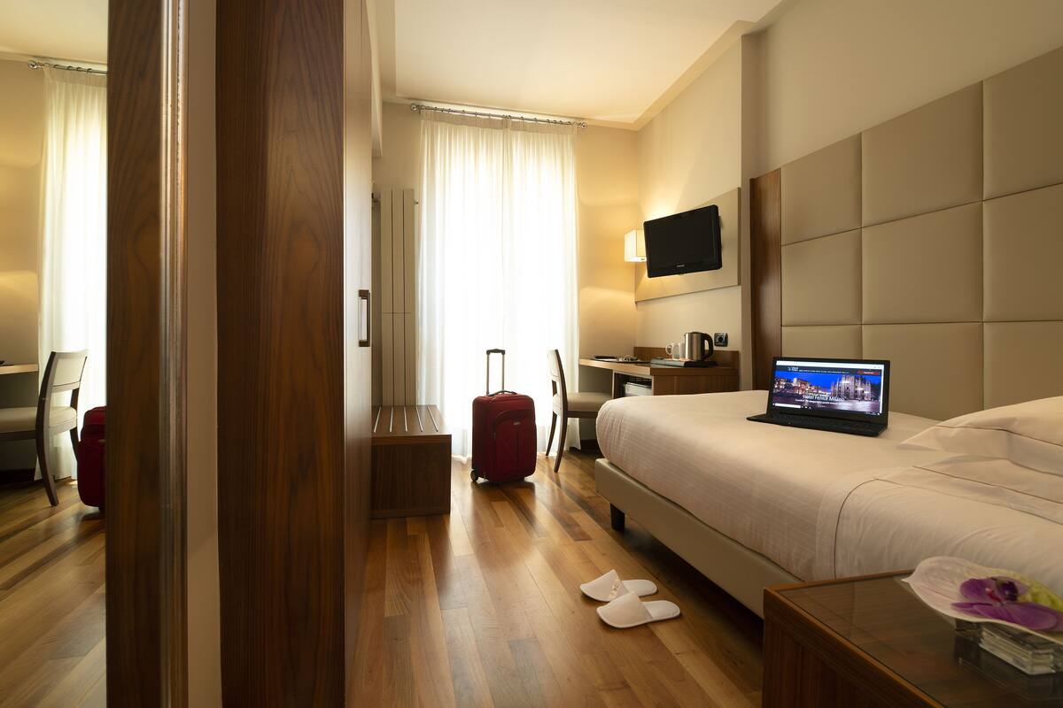 A hotel room with a bed, a desk, a chair, a TV, and a suitcase.