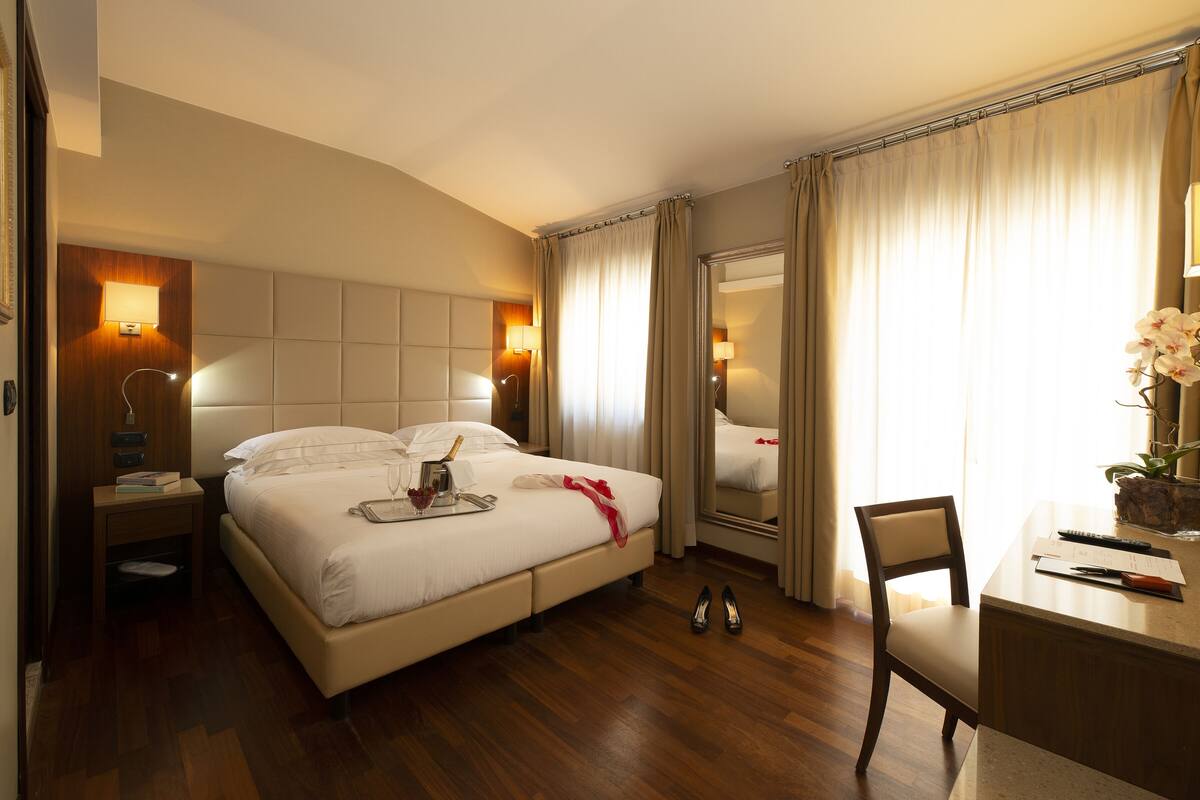 A hotel room with a large bed, a bedside table with a lamp, a dresser, a chair, and a mirror.