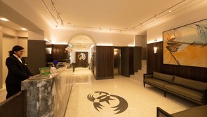 Zona de recepción de hotel con mostrador de mármol, un escritorio, un sofá y un cuadro abstracto de gran tamaño en la pared.