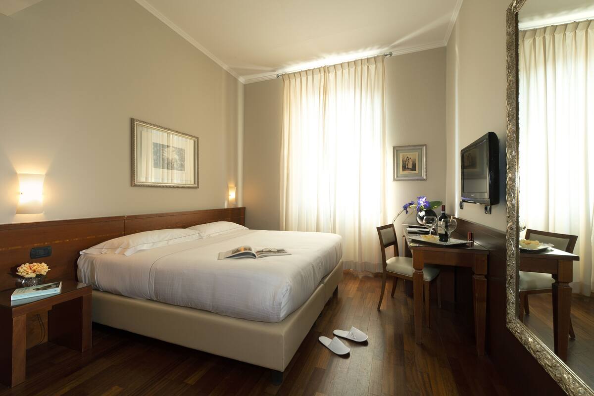 A hotel room with a large bed, a desk with a chair, a television, and a mirror.