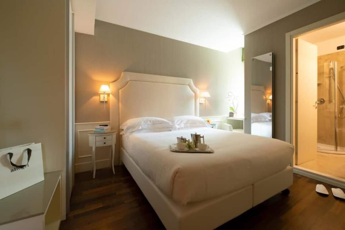 A hotel room with a bed, bedside table, lamp, and a shower area.