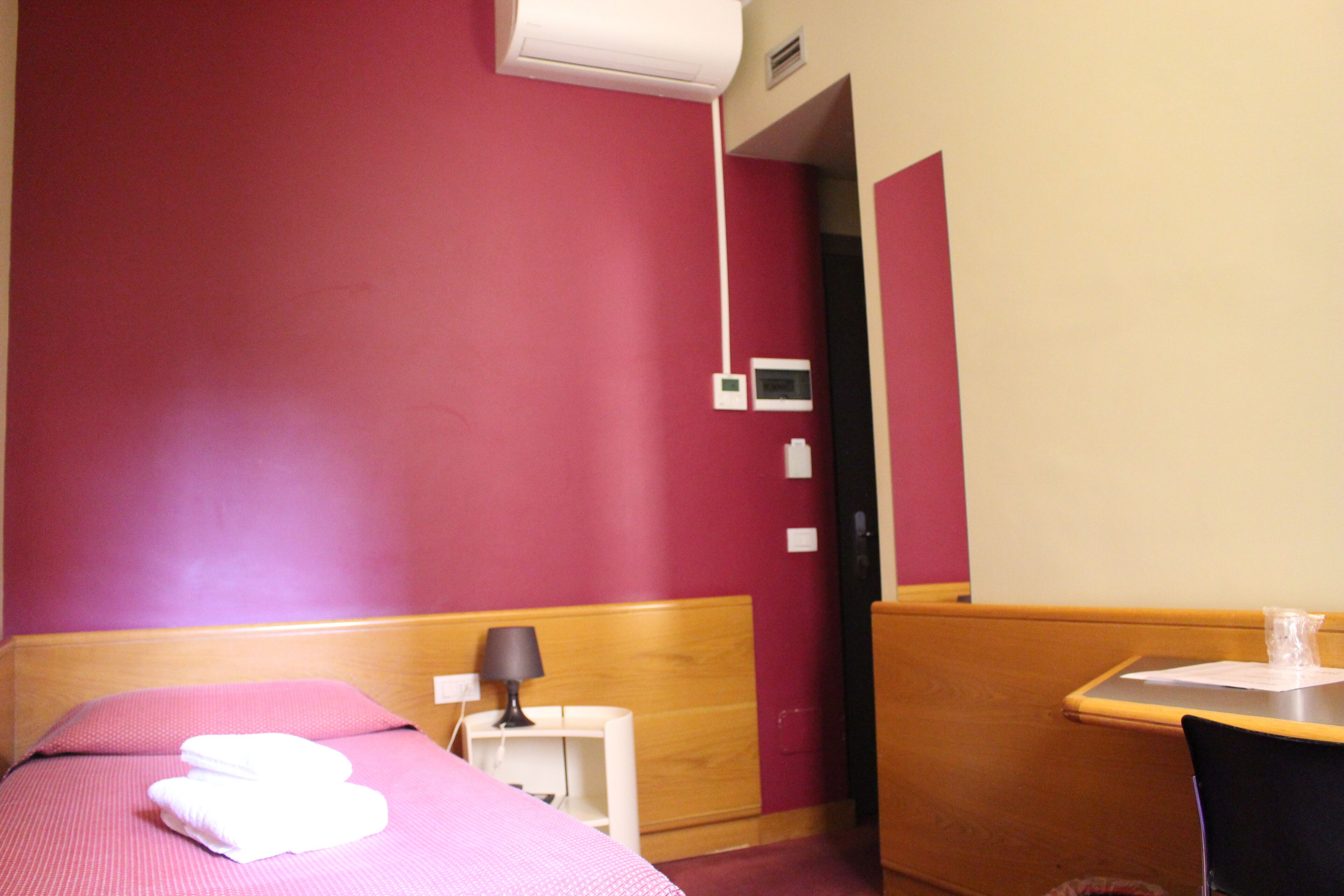 A hotel room with a bed, a small table, a chair, a lamp, and a bathroom door.