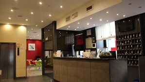 A modern hotel lobby with a reception desk, a red accent wall, and a seating area with green chairs. - Hotel Club (Milan)