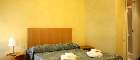 A hotel room with a bed, a nightstand, and a door.