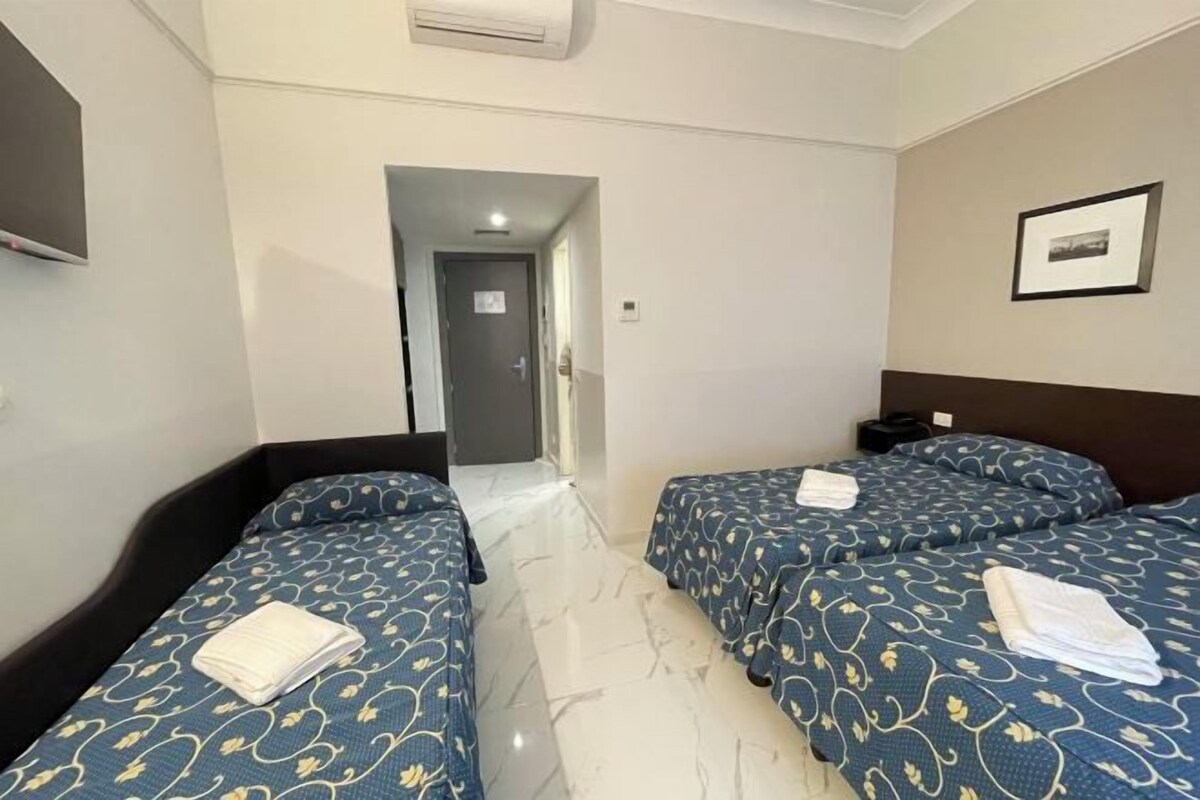 Habitació d'hotel amb dos llits, un televisor de pantalla plana, un quadre al mur i una porta que dona a una altra habitació.