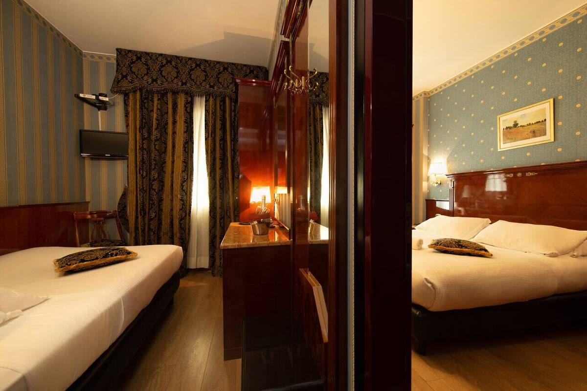 A hotel room with two beds, a desk with a lamp, a television, and a painting on the wall.