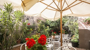 An outdoor patio area with a table and chairs under a canopy, surrounded by potted plants and a brick wall. - Hotel Vittoria (Milan)
