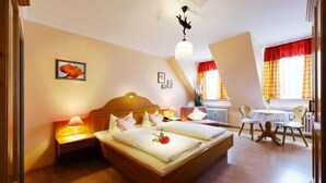A bedroom with a wooden bed, bedside lamps, a small table with chairs, and a window with curtains.