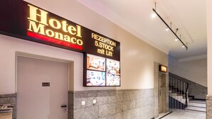 A hotel reception area with a sign for 'Hotel Monaco' and a 'RECEPTION 5.STOCK mit Lift' sign.