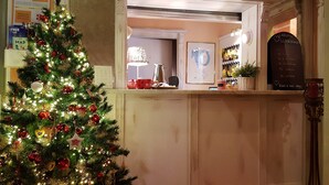 A Christmas tree with lights and ornaments, a reception desk with a lamp, a framed picture, and a signboard with a welcome message.