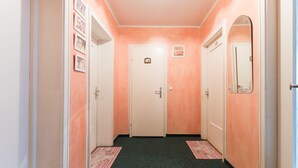 A hallway with peach-colored walls, white doors, and a green carpet. There are framed pictures on the left wall and a mirror on the right wall.