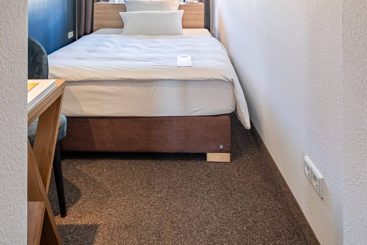 A hotel room with a bed, bedside table, lamp, and a large mirror.