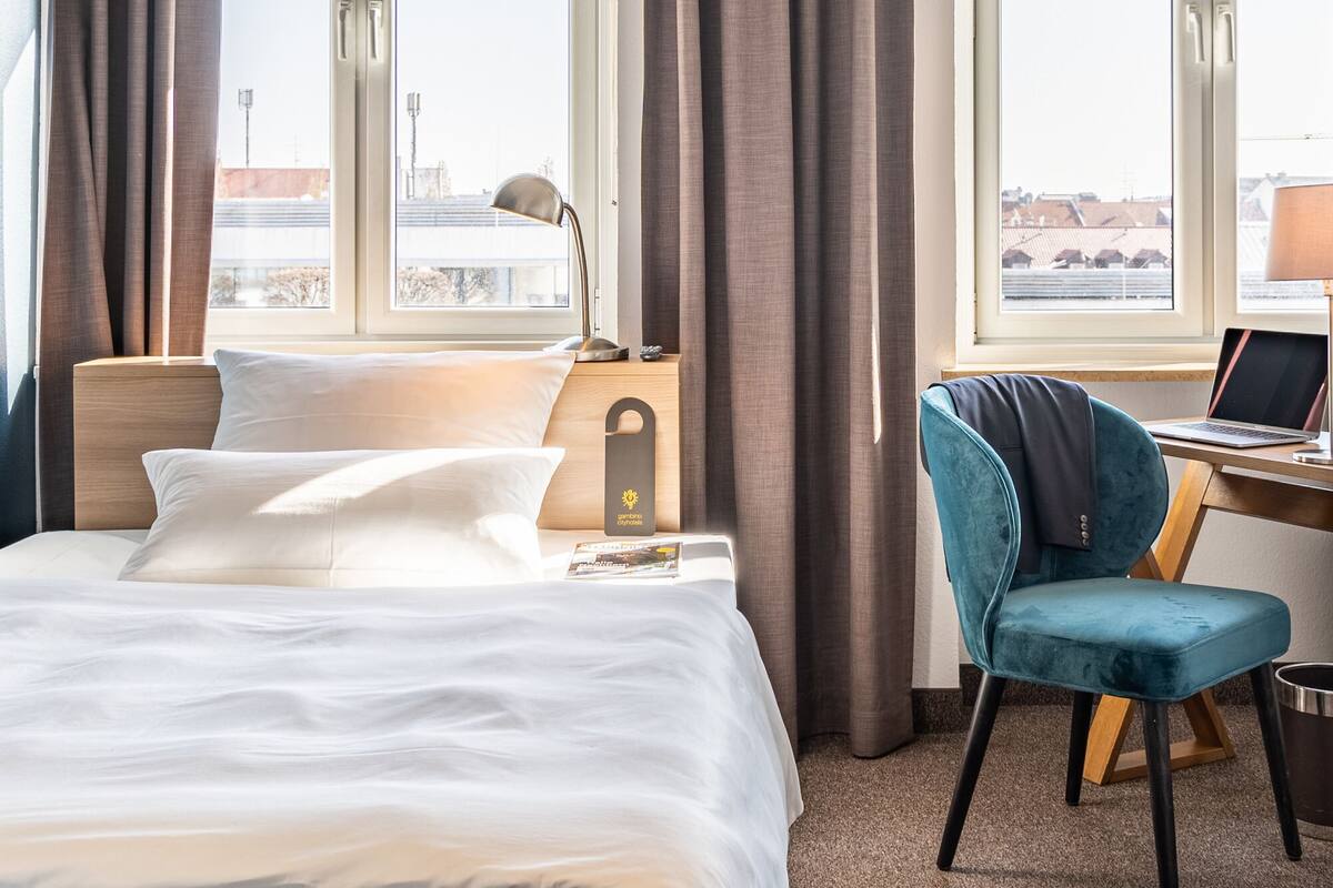 A hotel room with a bed, a desk with a laptop, a chair, and curtains.
