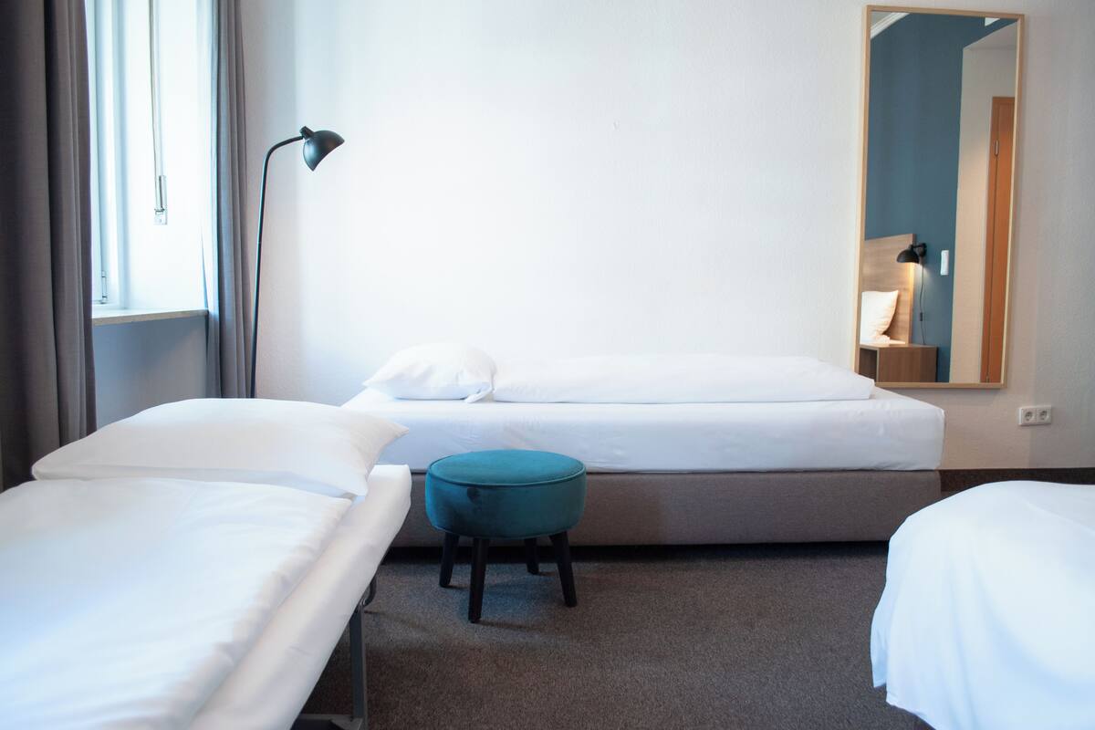 A hotel room with two beds, a small stool, a lamp, and a mirror.