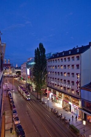 Ein Hotel mit mehreren Etagen, einem gut sichtbaren Eingang und einer Straße mit parkenden Autos und einer Straßenbahn.