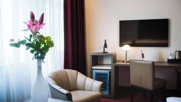 Habitación de hotel con escritorio, dos sillas, televisor, un florero con flores y un miniibar.
