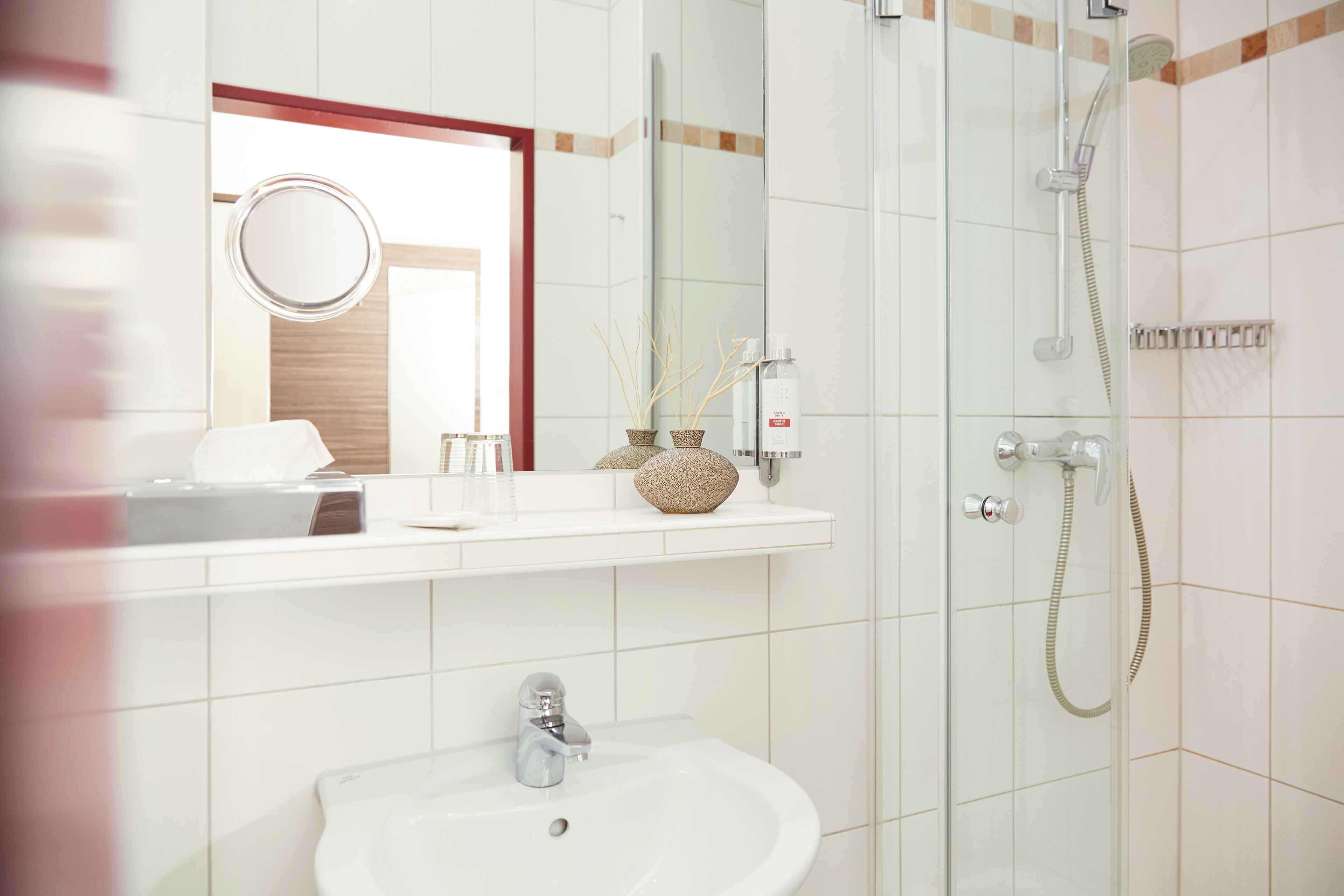 Une salle de bain équipée d’un lavabo, d’un miroir, d’une douche et d’un porte-serviettes.