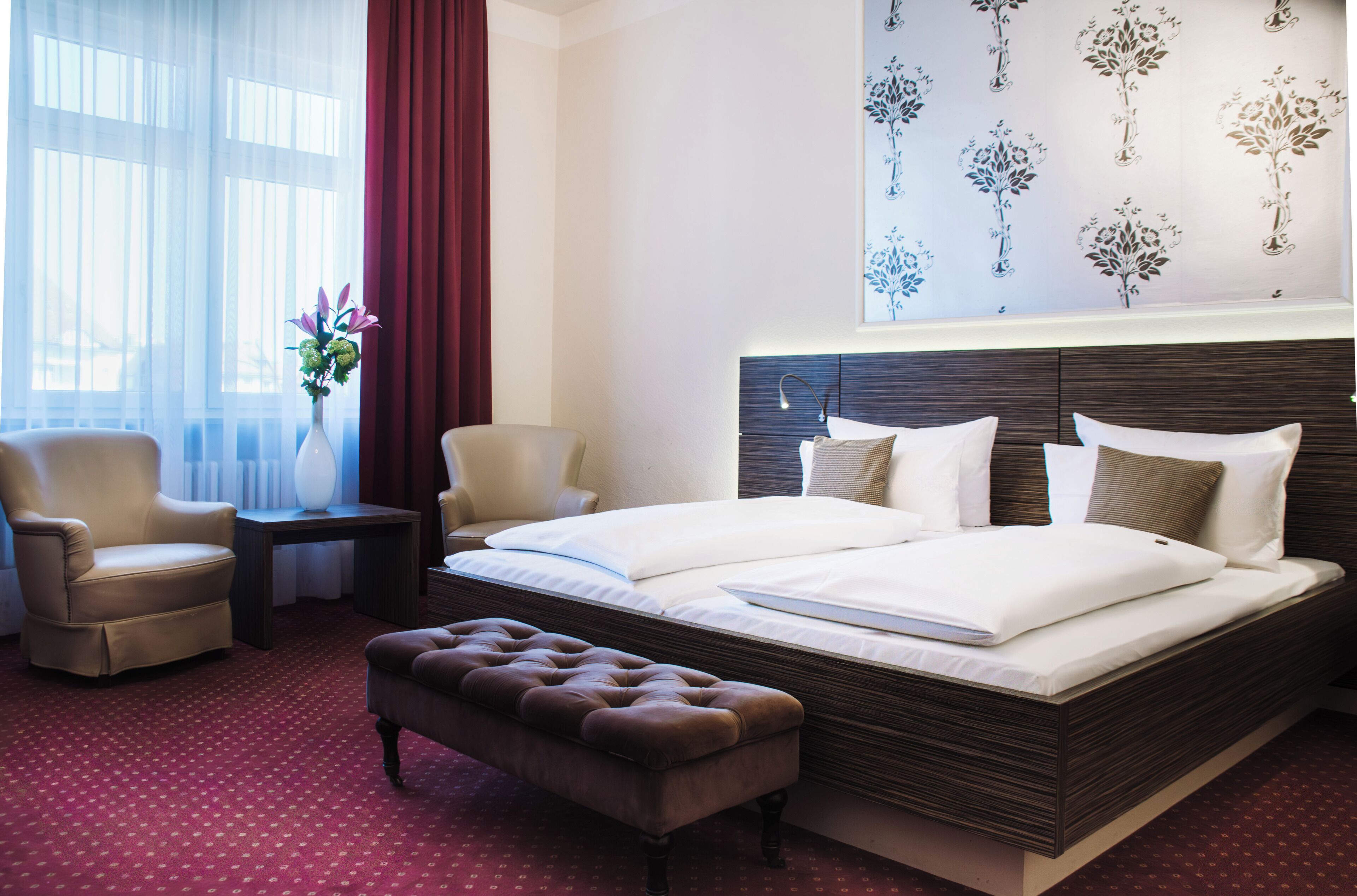 Ein Hotelzimmer mit einem großen Bett, zwei Stühlen, einem kleinen Tisch und einer Wandverzierung.