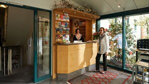 Un mostrador de recepción con encimera de madera, separador de vidrio y vistas al exterior a través de amplias ventanas.