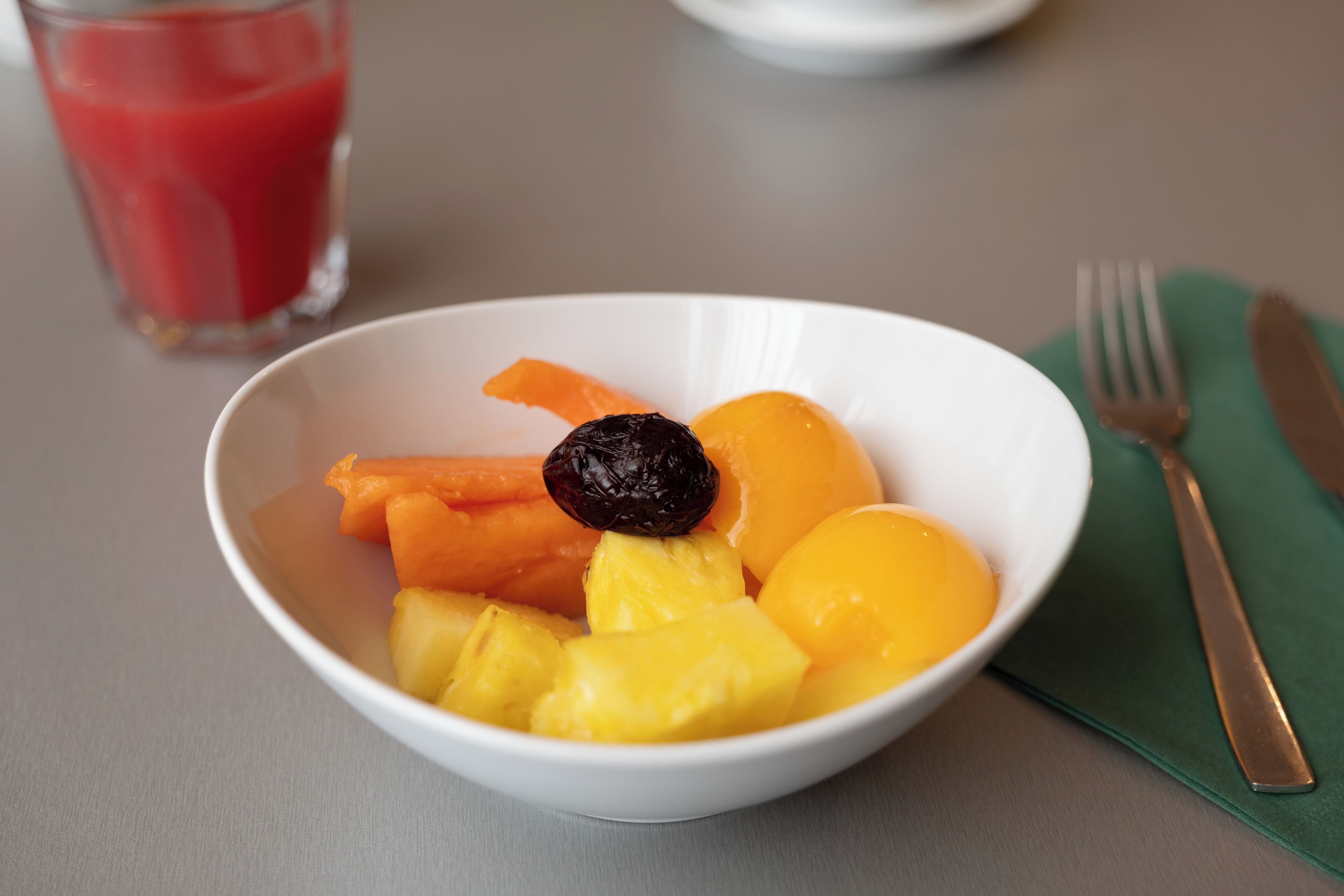 A bowl of fruit with a glass of red juice in the background.