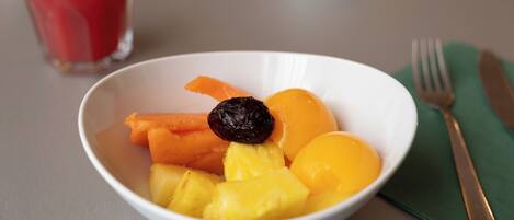 A bowl of fruit with a glass of red juice in the background.