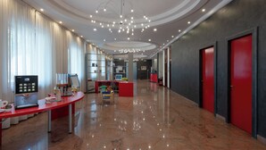 Un hall d’hôtel moderne avec un comptoir d’accueil incurvé, un espace dédié au café et un coin salon.