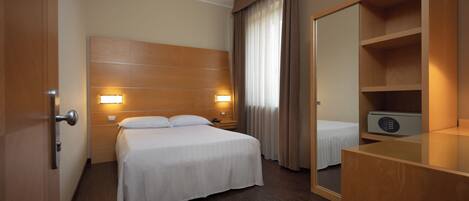 A hotel room with a wooden headboard, a bed with white bedding, a bedside table with a lamp, a mirror, and a wardrobe.