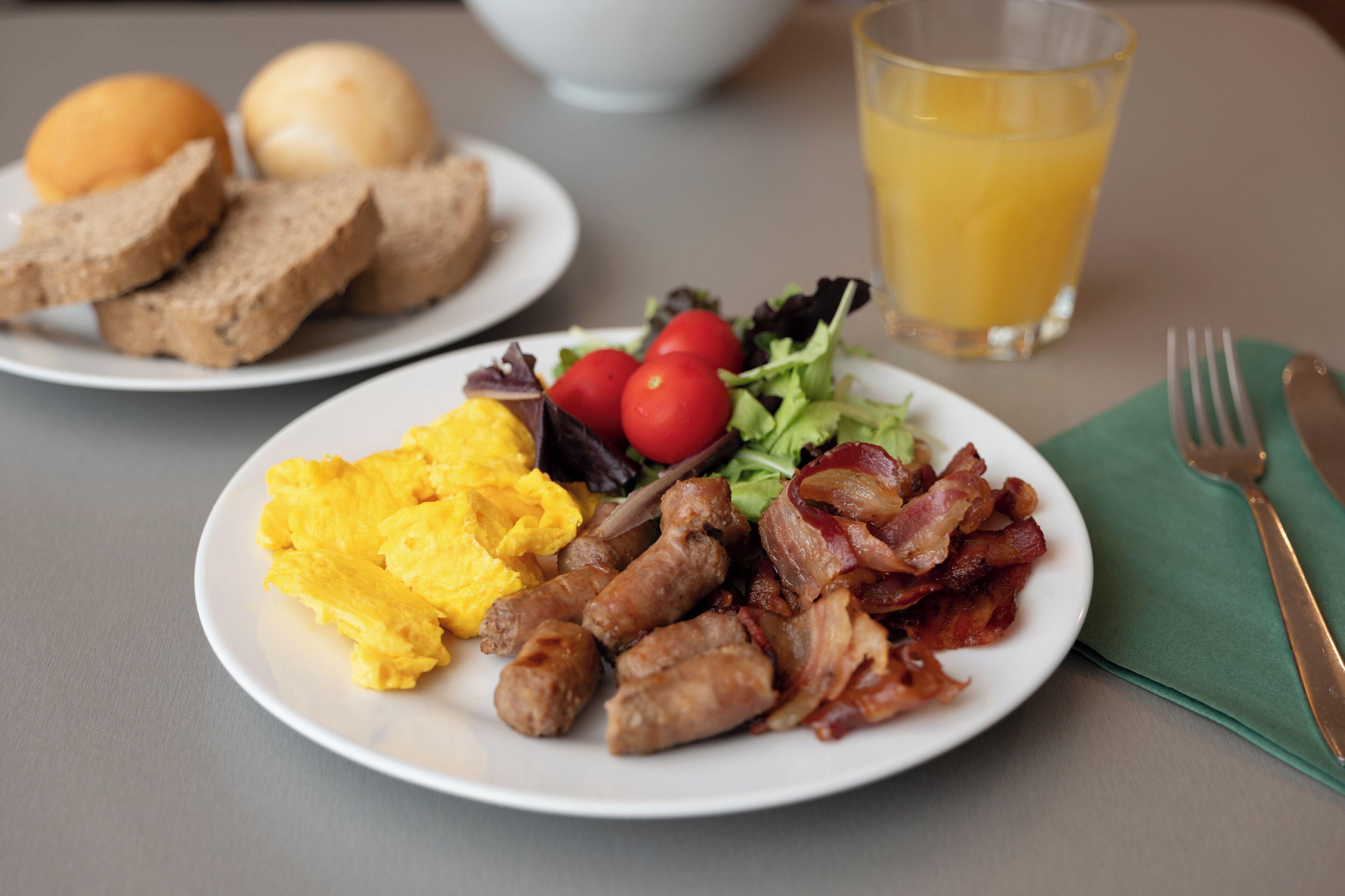 En frukosttallrik med äggröra, korv, bacon och en liten sallad.