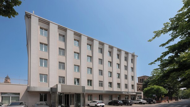 Un hôtel à plusieurs étages, doté d’une façade moderne, d’une entrée en verre et de plusieurs voitures garées devant.