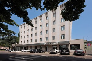 Un hotel de varios pisos con fachada moderna, un acceso cubierto y varios coches aparcados.