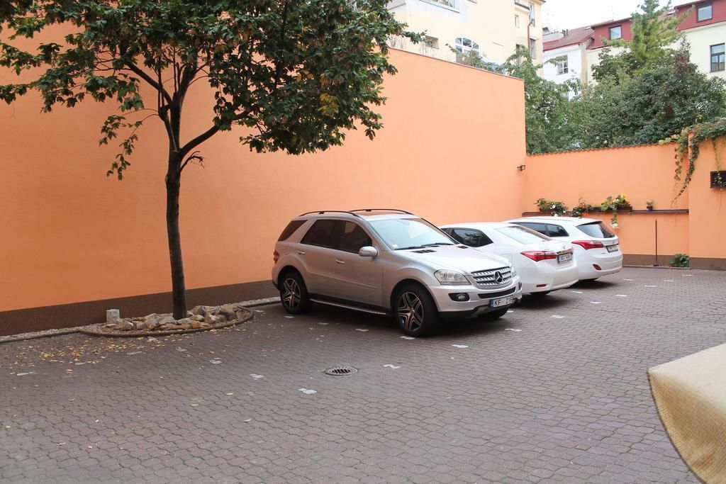 A parking area with two cars parked next to a tree and a building with an orange wall.