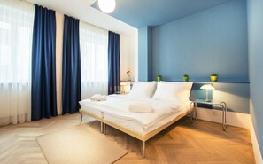 Una habitación de hotel con cama, mesita de noche con lámpara y ventana con cortinas.
