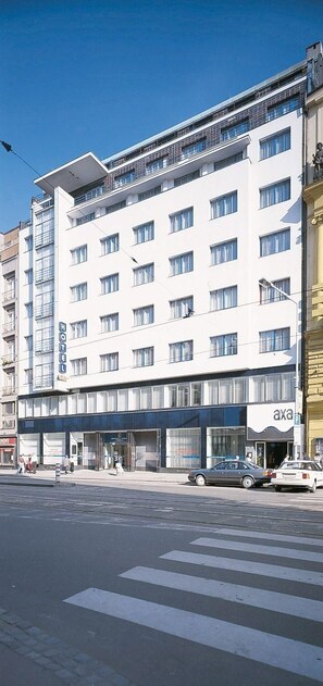 A multi-story hotel with a modern facade, a visible ground floor with a storefront, and a clear pedestrian crossing in the foreground. - Hotel Axa Prague (Prague)