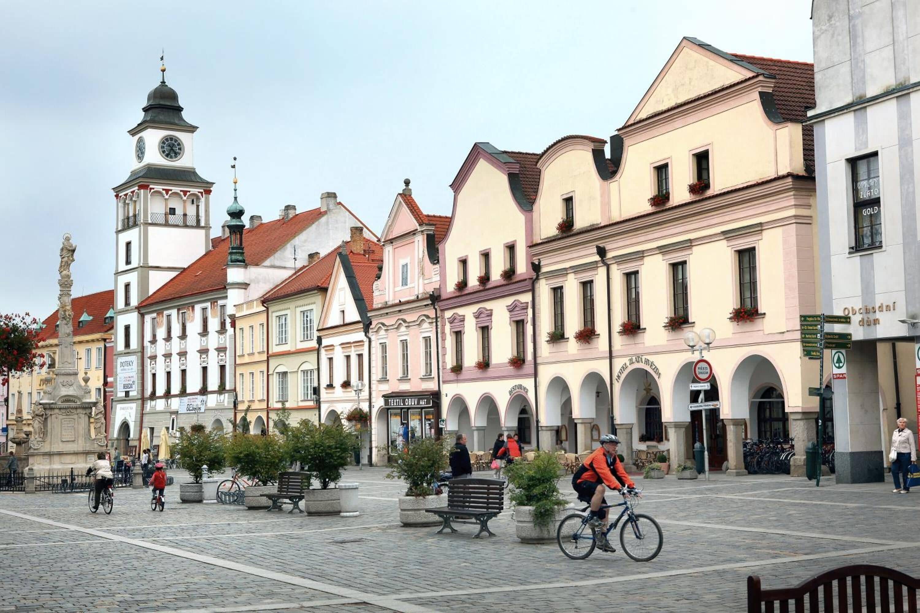 Una plaza adoquinada con edificios históricos, una torre del reloj y una estatua.