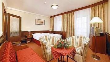 A hotel room with a bed, two armchairs, a small table with a flower arrangement, a desk, and a lamp.