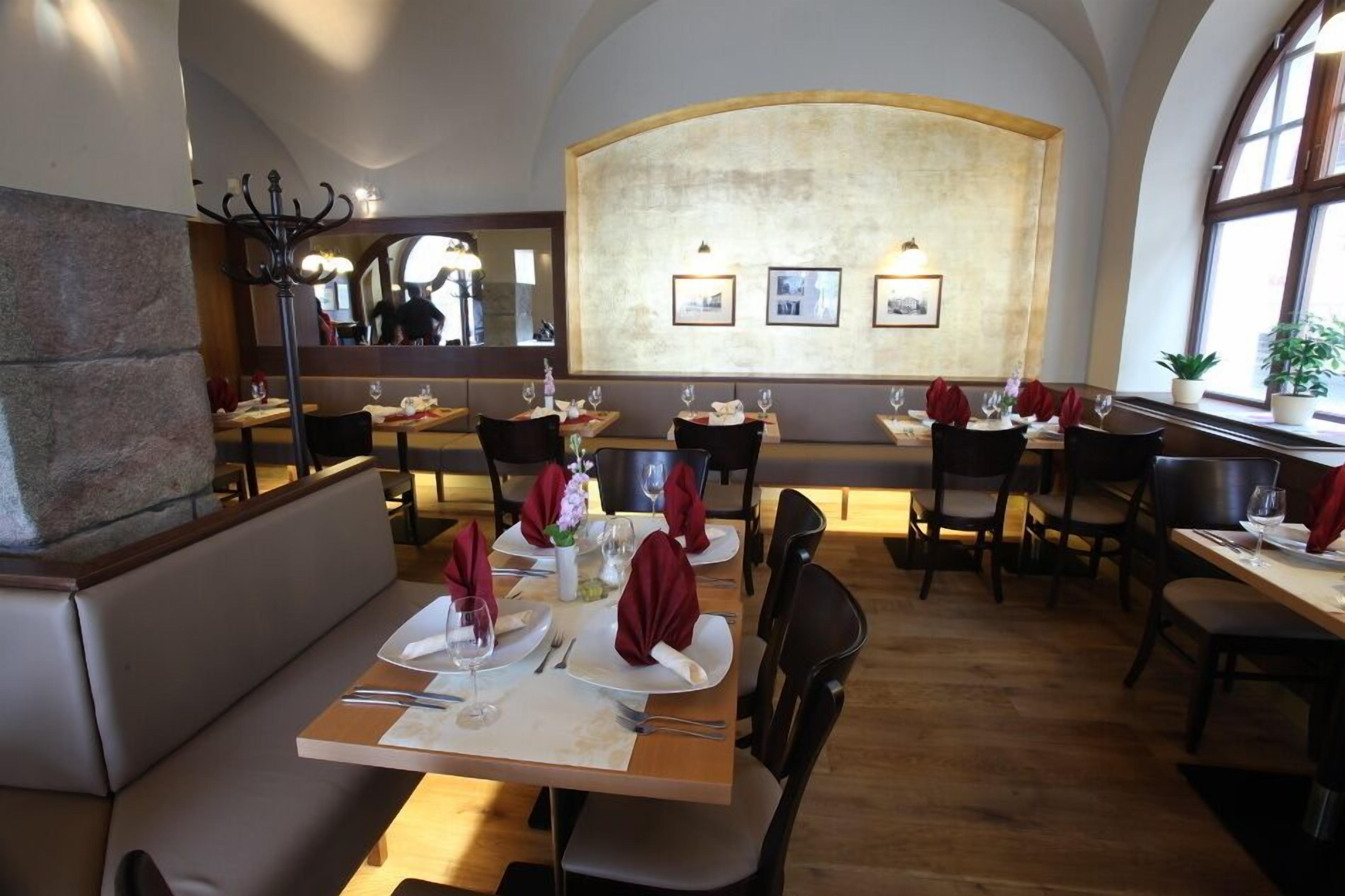 Un restaurante con un techo alto en arco, mesas de madera dispuestas con servilletas rojas y cuadros enmarcados en la pared.