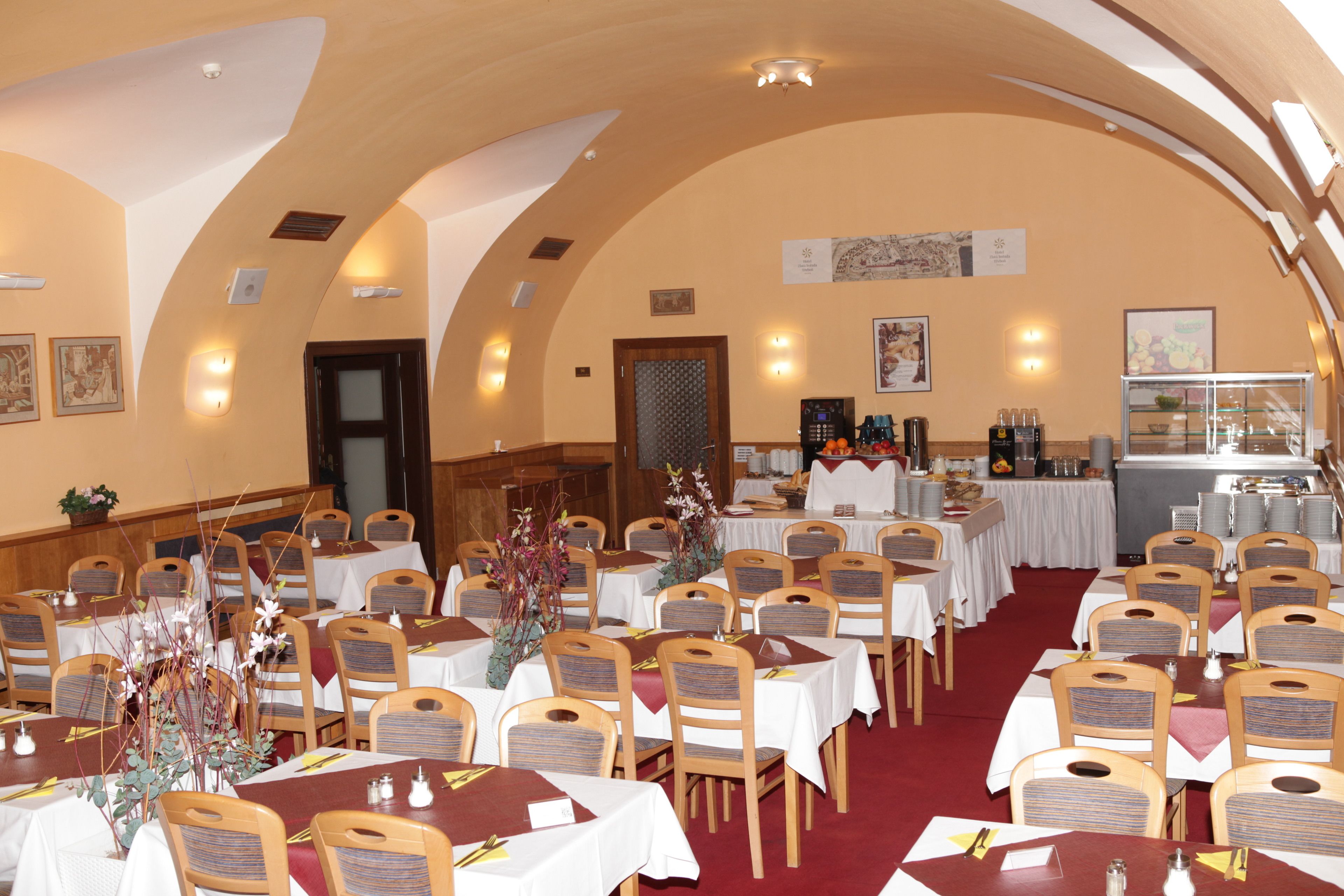 Een feestzaal met meerdere tafels en stoelen, gerangschikt in rijen, en een centraal buffet.