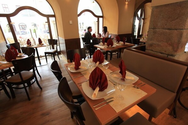 A restaurant with tables set for dining, featuring a stone wall and arched windows.