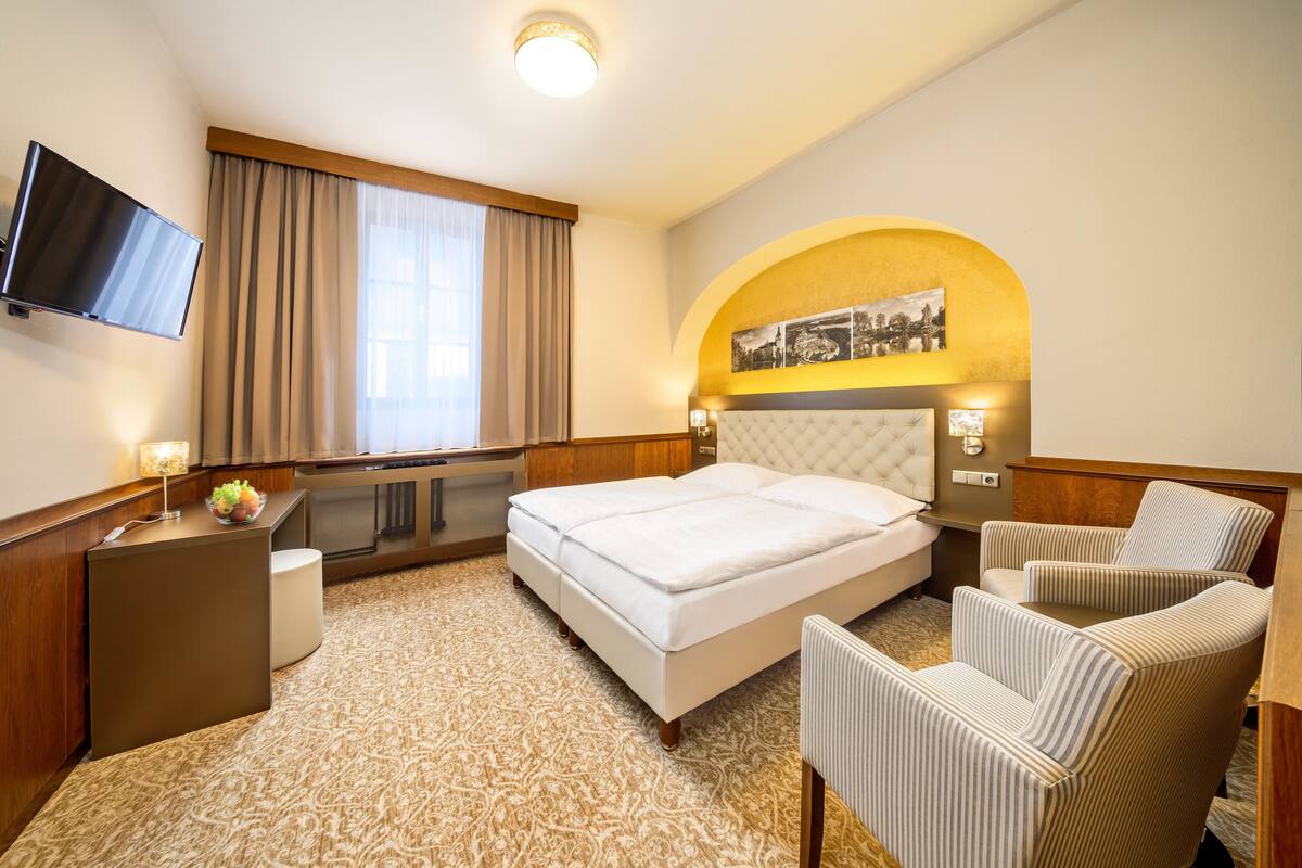 A hotel room with a bed, a desk, a television, a chair, and a window with curtains.