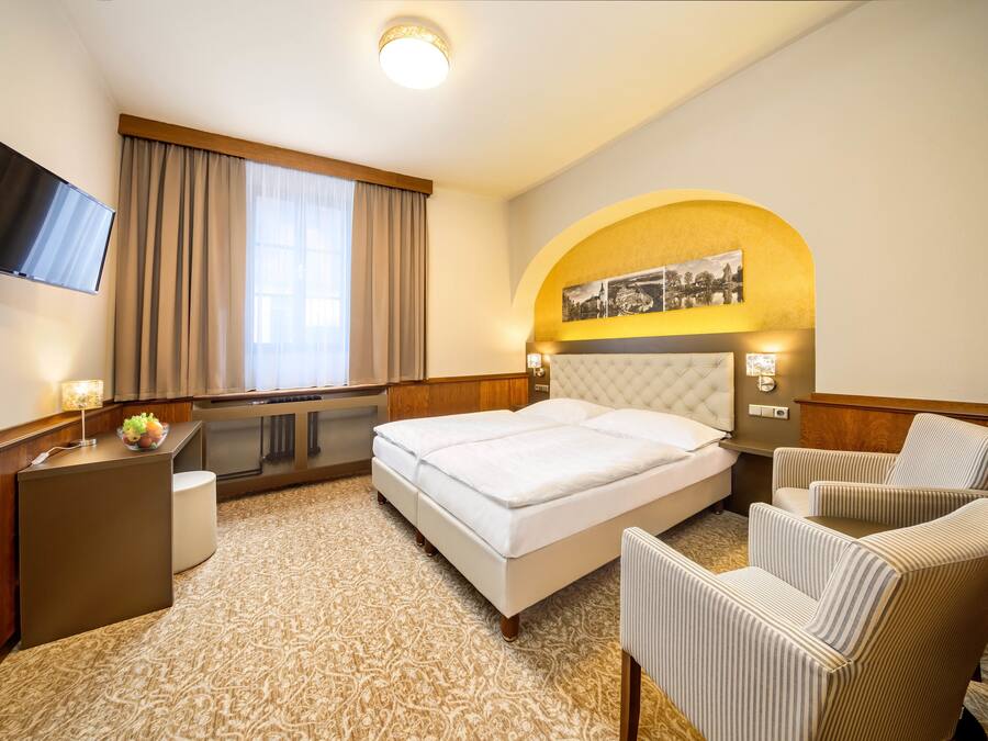 Habitación de hotel con cama, escritorio, televisor, silla y ventana con cortinas.