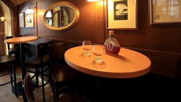 Un restaurante tenuemente iluminado con paredes de madera, mesas redondas y sillas. Hay cuadros enmarcados en la pared y una botella de licor sobre una de las mesas.