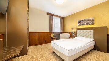 Habitación de hotel con una cama grande, televisión, una mesita con lámpara y ventana con cortinas.