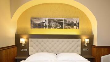 Een hotelkamer met een gestoffeerd hoofdeinde, twee nachtkastjes met lampen, en een wanddecoratie met een landschap.