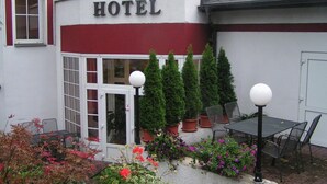 L'ingresso di un hotel con facciata rosso e bianco, una porta in vetro e piante in vaso.