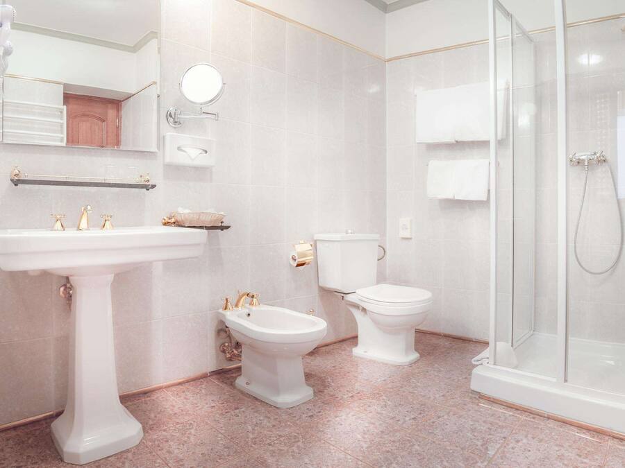 A bathroom with a pedestal sink, a bidet, a toilet, and a glass-enclosed shower.